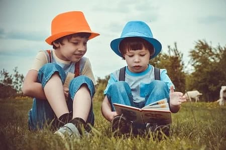 Deux enfants assis dans l’herbe lisant un livre, illustrant la fratrie et les liens familiaux liés aux tests de paternité