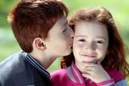 Deux enfants assis dans l’herbe lisant un livre, illustrant la fratrie et les liens familiaux liés aux tests de paternité